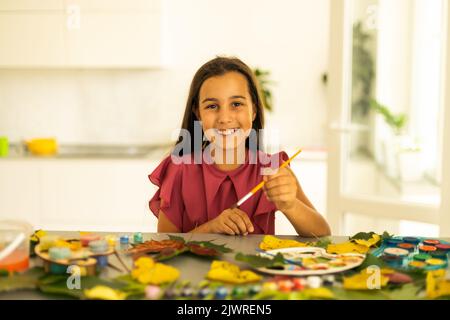 child paints leaves with paints, draws a picture, making prints of leaves. Childrens creativity in nature. Outdoor. Summer. Stock Photo