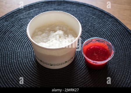 Rice flake porridge in a white round carton take-away box with fresh strawberry jam. Stock Photo