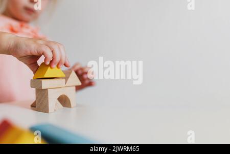 Adorable little child girl of preschooler age playing wooden building blocks at home or kindergarten. Toddler kid is stacking a tower from colourful cube toys on the table. Kids Play Room. Banner size