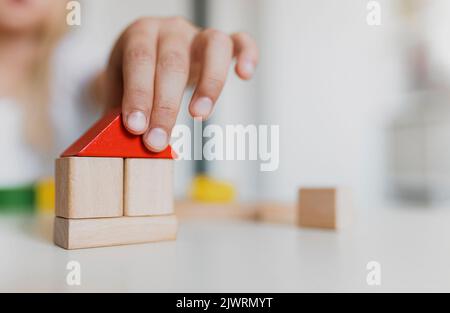 Little child girl of preschooler age playing wooden building blocks at home or kindergarten. Kid is stacking tower from colourful toys on table. Kids Play Room. Development, construction concept