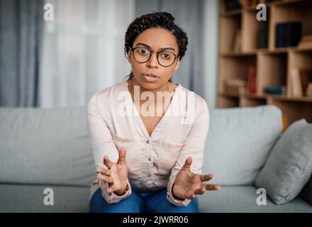 Serious young black woman doctor in glasses speaks and gesticulates, looking at camera in office Stock Photo