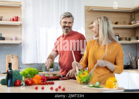 Loving spouses preparing healthy meal together, kitchen interior Stock Photo