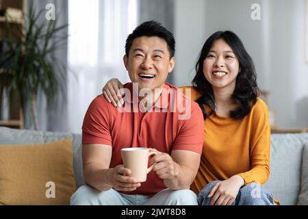 Positive asian husband and wife watching movie, drinking tea Stock Photo