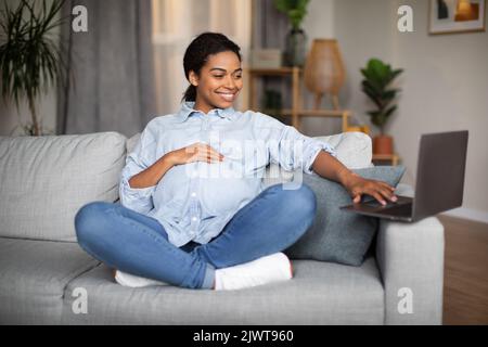 Happy pregnant african woman using laptop working online at home Stock Photo