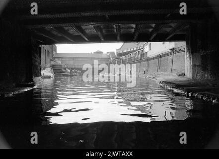 London, England, circa 1967. A view of the Regent’s Canal from under Oval Road bridge. Ahead is the railway bridge adjacent to Gloucester Avenue and the disused premises of the gin distillers, W & A Gilbey. Children of The Pirate Club are playing aboard boats and to their left is ‘Rosedale’, a disused barge which served as their clubhouse. The Pirate Club, a children’s boating club was formed in 1966 at Gilbey’s Wharf on the Regent’s Canal near Camden, London. A number of small boats and canoes had been donated for the children’s use. Stock Photo
