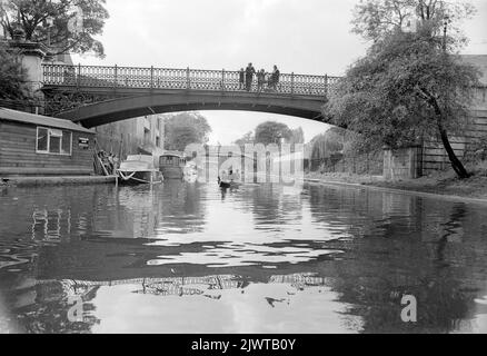 London, England, circa 1967. A family standing on The Broad Walk footbridge over the Regent’s Canal at Cumberland Basin are watching boys of The Pirate Club paddling a boat below them. Ahead is London Zoo’s Snowdon Aviary in Regent’s Park. The Pirate Club, a children’s boating club was formed in 1966 at Gilbey’s Wharf on the Regent’s Canal near Camden, London. Their clubhouse was an old barge and a number of small boats and canoes had been donated for the children’s use. Stock Photo