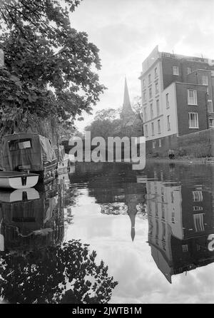 London, England, circa 1967. A view from the Regent’s Canal near Camden, London. Ahead is a building situated in St Mark’s Square and Regent’s Park Road bridge. In the distance is the spire of St. Mark’s Church. Boats are moored on the canal and a couple are walking along the towpath. Stock Photo
