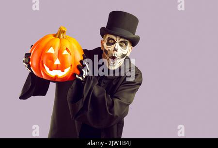 Funny surprised man in skeleton Halloween costume holding jack o lantern and looking at camera Stock Photo