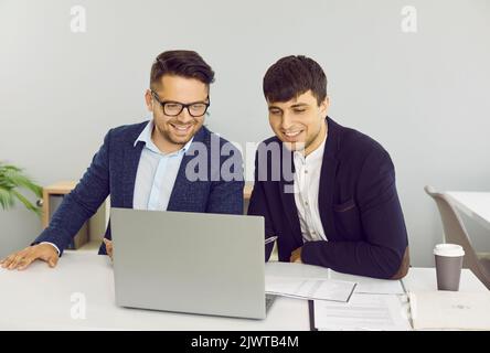 Two friendly male colleagues are working together in office on joint startup project. Stock Photo