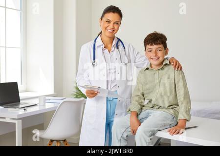 Smiling pediatrician doctor woman is cuddling teen boy on appointment in clinic with care. Stock Photo