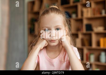 Sad bored pretty schoolgirl pupil studying at home, resting head on hand and looking at camera Stock Photo