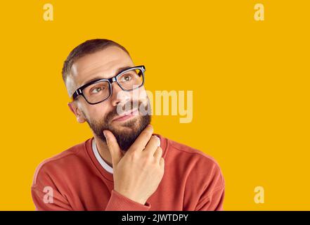 Young man in eyeglasses looking away at yellow copy space background and thinking Stock Photo
