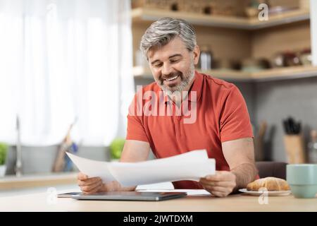 Handsome middle aged businessman working from home, reading papers Stock Photo