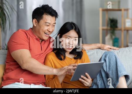 Happy asian lovers using digital tablet, home interior Stock Photo