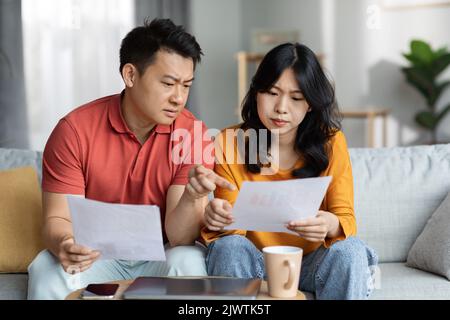Confused asian spouses checking bills, home interior Stock Photo