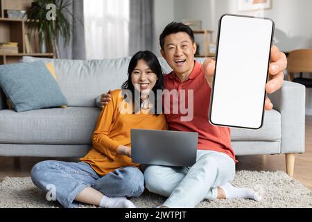 Emotional chinese couple chilling together at home, using gadgets Stock Photo