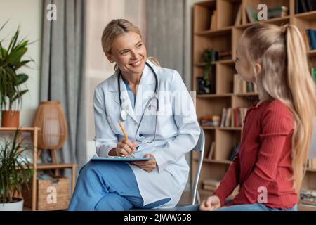 Friendly female doctor pediatrician talking to little girl patient at checkup consultation, pediatrist consulting kid Stock Photo