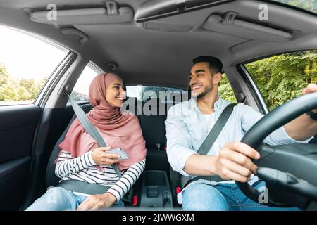 Cheerful young middle eastern woman in hijab with smartphone and husband rides on car Stock Photo