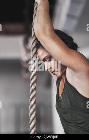 Composing herself for the rest of the climb. a young woman climbing a rope at the gym. Stock Photo