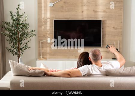 cheerful couple turns on the TV while lying on the sofa in the living room Stock Photo
