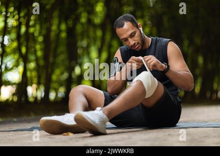 African american sportsman wrapping injured knee with elastic bandage Stock Photo