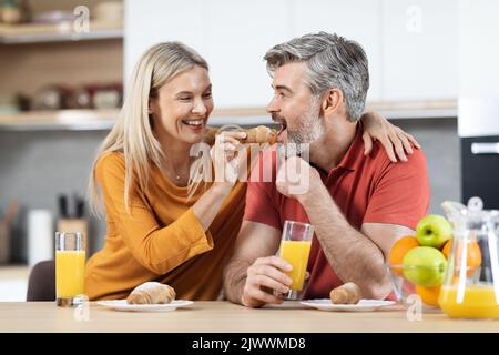 Positive blonde woman feeding her handsome spouse Stock Photo