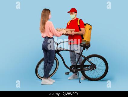 Male Courier Delivering Pizza Boxes To Woman On Blue Background Stock Photo