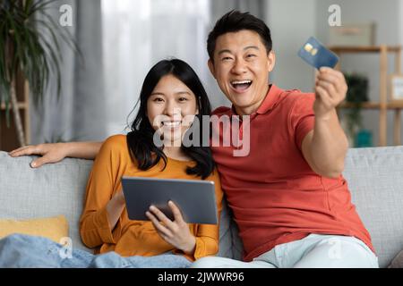 Happy asian husband and wife using tablet and credit card Stock Photo