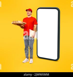 Cheerful Deliveryman Holding Pizza Boxes Standing Near Smartphone, Yellow Background Stock Photo