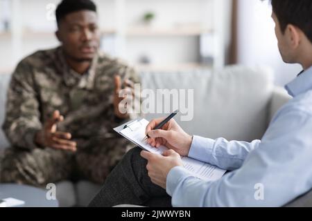 Psychologist taking notes while having conversation with black soldier Stock Photo