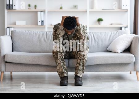 Stressed african american soldier in military uniform sitting on couch Stock Photo