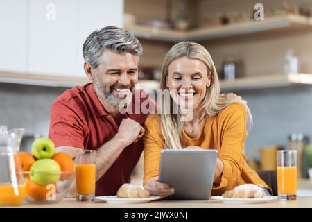 Loving couple enjoying healthy breakfast, using digital tablet Stock Photo