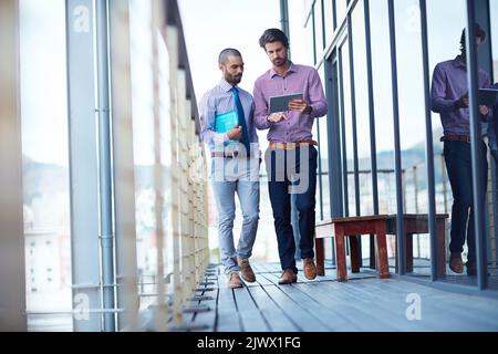 Staying updated in between meetings. two young businessmen using a digital tablet together outside of an office building. Stock Photo