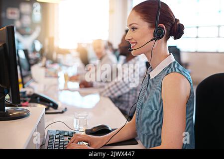 Answering your call with a smile. a happy call center agent working at her computer in the office. Stock Photo