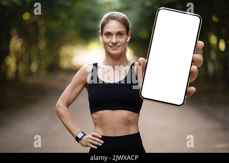 Cheerful young athletic woman showing smartphone, mockup Stock Photo