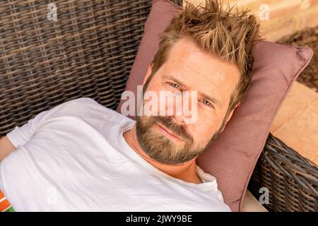 Close up young handsome man lying on sofa at the terrace. Stock Photo