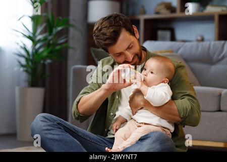 A young father, with a child, does housework. Father on maternity leave. Dad cheerfully sings, dances and vacuums, cleans with a small child in his Stock Photo