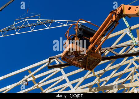 A worker nails the beams of the rafters of a home's roof with an air hammer in the construction of a household. Stock Photo
