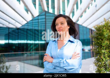 Confidence Businesswoman portrait with crossed hands. Pretty business woman 30 years old standing near office building dressed blue shirt. Caucasian female business person outside Stock Photo