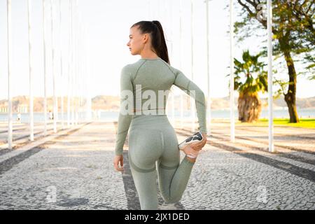 Woman Stretching And Warming-Up Legs Before Running. Fit sport woman stretching her body warm up before workout outdoor. Girl in sportswear exercises outside in summer park for health and wellbeing. Stock Photo