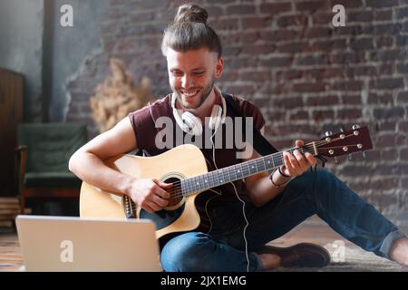 Caucasian young adult learning guitar online music class with distant teacher computer mobile device. Handsome hipster man teaching music through laptop, distance education learning concept Stock Photo