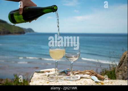 Pouring of txakoli or chacolí slightly sparkling very dry white wine produced in Spanish Basque Country, served outdoor with view on Bay of Biscay, At Stock Photo