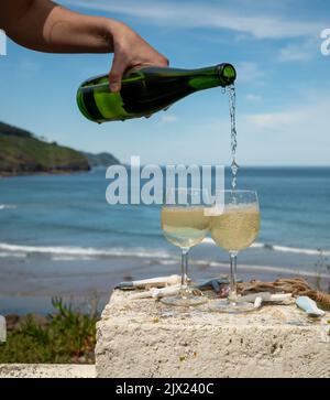 Pouring of txakoli or chacolí slightly sparkling very dry white wine produced in Spanish Basque Country, served outdoor with view on Bay of Biscay, At Stock Photo