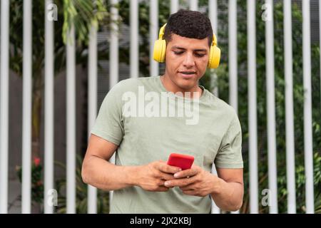 Young Man In Headphones Using Mobile Phone At City Street Stock Photo