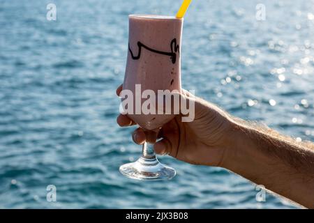 Close up first person view of male hand holding glass of cold icy milkshake Stock Photo