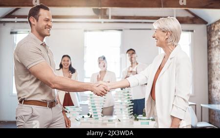 Architect, business handshake and partnership meeting of people in agreement for architecture plan at the office. Happy senior woman and young man Stock Photo