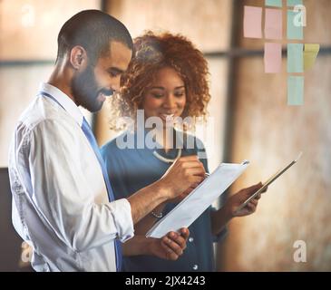 Entrepreneurs doing what they do best. two young professionals brainstorming with sticky notes on a glass wall in an office. Stock Photo