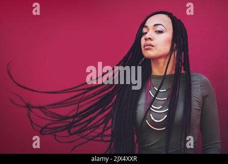 Let your style reflect your attitude and personality. a young woman with braids posing against a pink background. Stock Photo