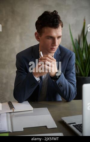 Young businessman in dark blue suit checking reports on laptop screen Stock Photo