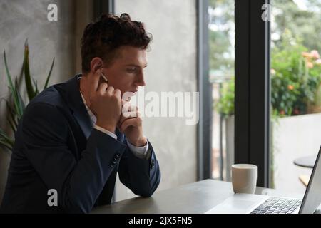 Serious young entrepreneur wearing earbuds when calling business partner Stock Photo